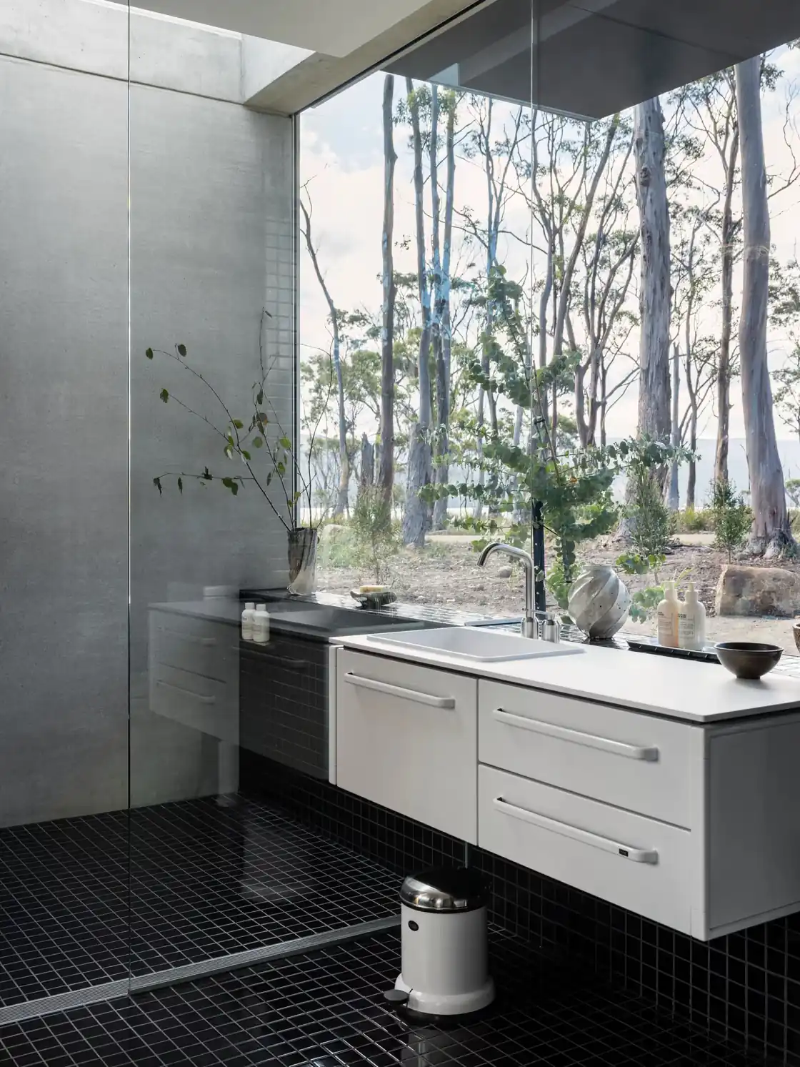 Bathroom with a white Vipp module, black tiles and a view of the trees
