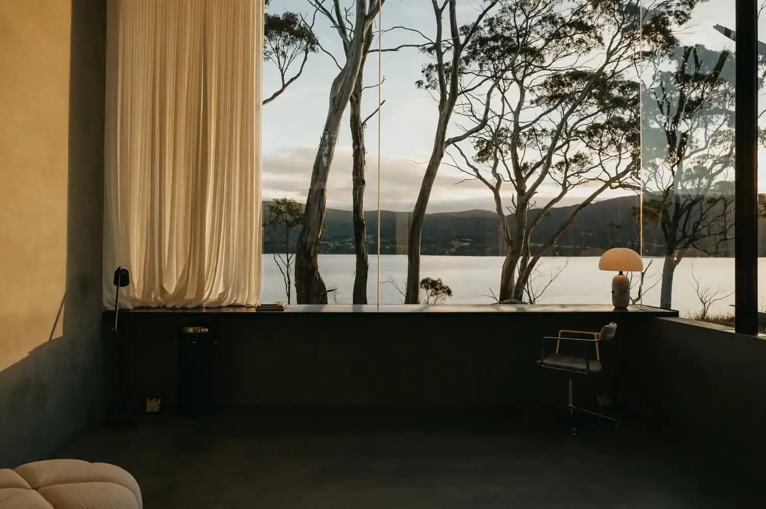 Studio desk with a lamp and linen curtains, facing gum trees and the channel