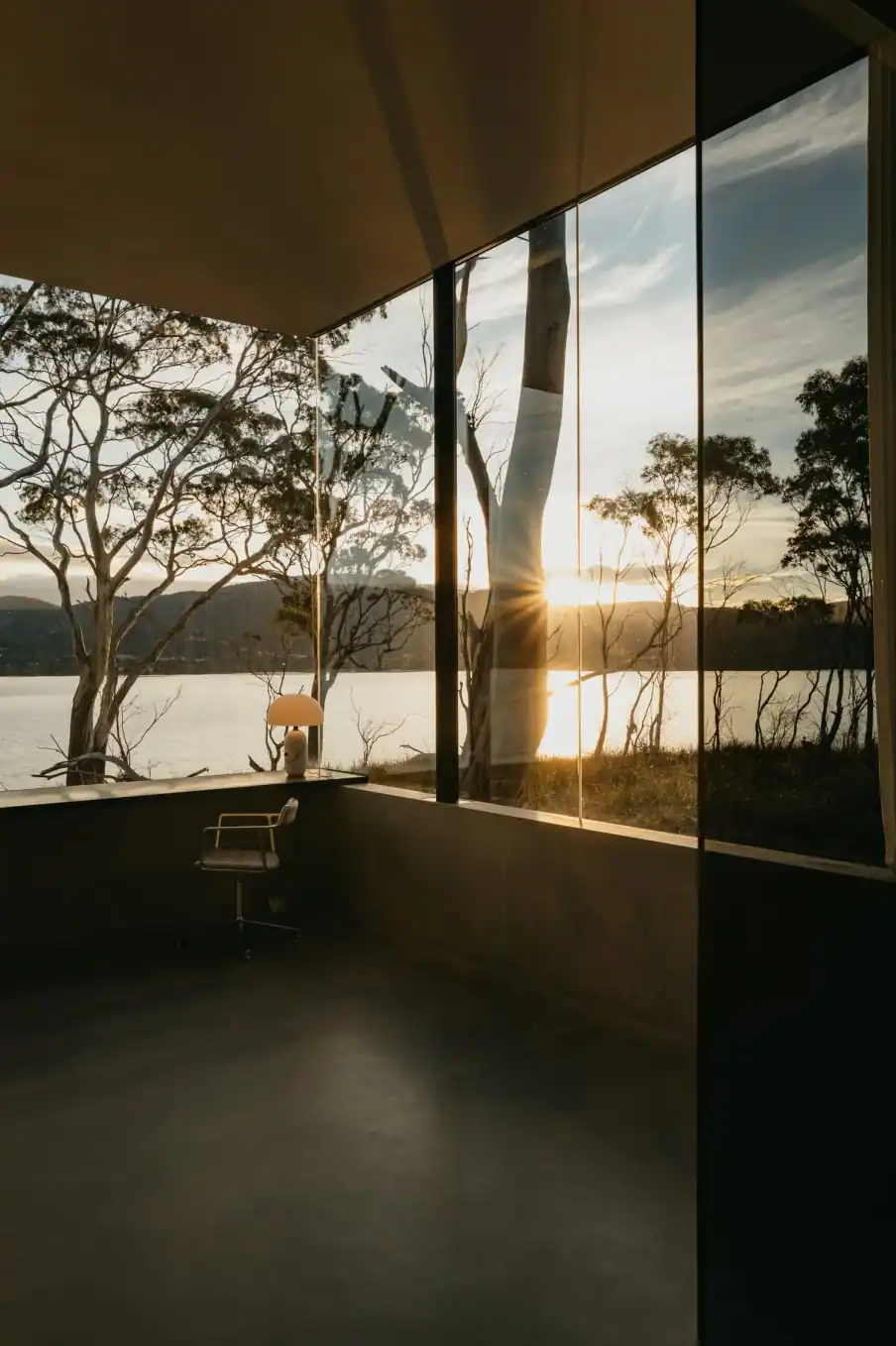 Tall studio window looking through gum trees to the channel at sunset